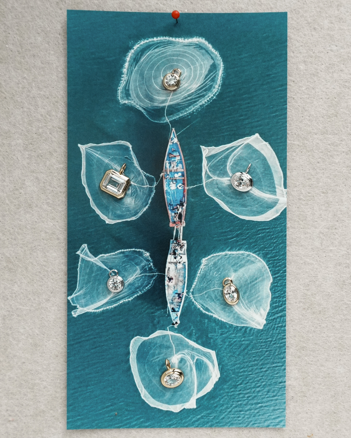Aerial view of a boat on teal water with six circular fishing nets, each holding a dazzling Tove Sapphire Bezel Charm by Mod + Jo, creating an artistic and visually striking scene.
