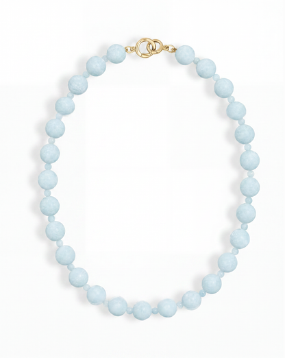 The Portia Gemstone Necklace by Mod + Jo features a single strand of round, light blue natural aquamarine beads with a gold clasp, displayed on a white background.