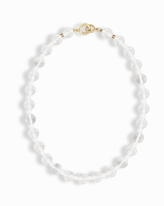 The Mod + Jo Portia Gemstone Necklace showcases round crystal quartz beads and a gold toggle clasp, arranged in an oval shape on a white background with soft shadows.