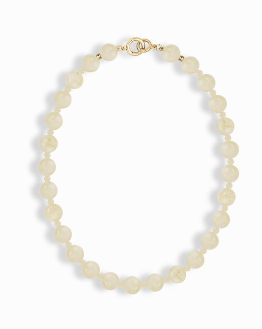 The Portia Gemstone Necklace by Mod + Jo features round, off-white pearl beads and a 14k gold-plated clasp, arranged in an oval shape on a white background.