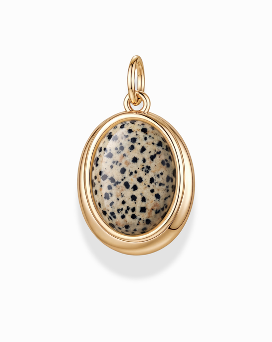The Rory Gemstone Charm by Mod + Jo features an oval polished Dalmatian Jasper stone with a beige base and black spots, set in a smooth 14k gold over brass bezel with a top loop for easy attachment to a necklace.