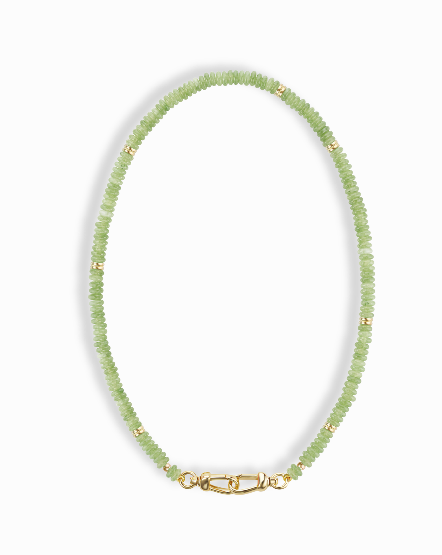 The Sonia Gemstone Necklace by Mod + Jo features small, round, light green genuine gemstone beads with gold spacers and a gold clasp, elegantly arranged in an oval shape against a white background.
