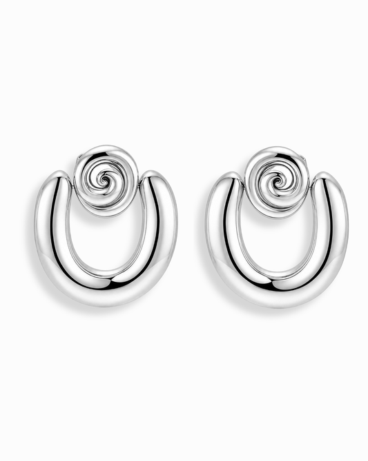 The Sabine Statement Earrings by Mod + Jo are shiny silver U-shaped hoops with a spiral design at the top, shown on a white background.
