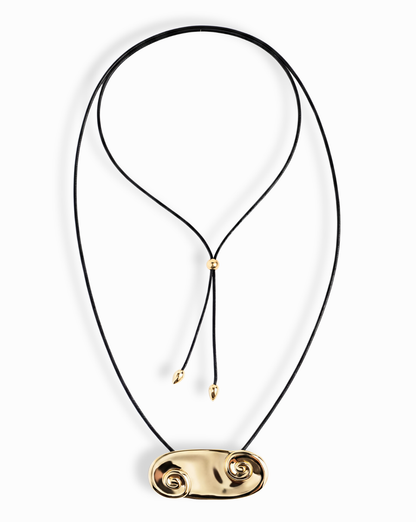 The Suna Spiral Cord Necklace by Mod + Jo features a black cord with an adjustable bolo closure, a sculptural 14k gold pendant with spiral shapes at each end, and two small gold beads on the cord ends.