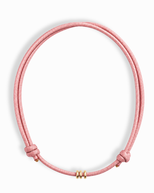 The Tommy Cord Necklace by Mod + Jo features a pink paracord with three gold-plated spacers at the front and adjustable side knots, shown against a white background.