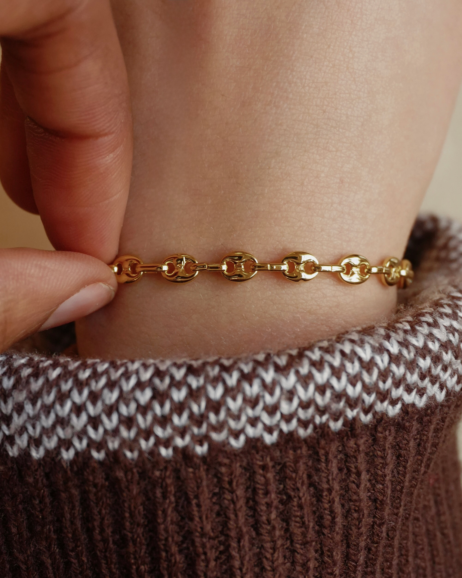 Gold bracelet on a wrist with a brown and white knit sleeve