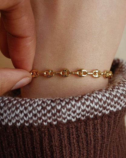 Gold bracelet on a wrist with a brown and white knit sleeve