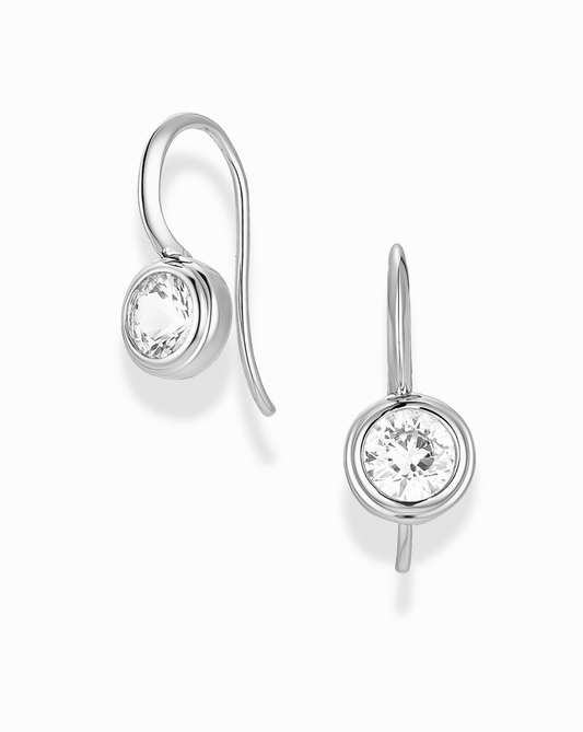 Silver earrings with round bezel sapphire gemstones in the center on a white background