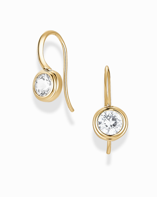 Gold round bezel earrings with a french hook and sapphire gemstones on a white background
