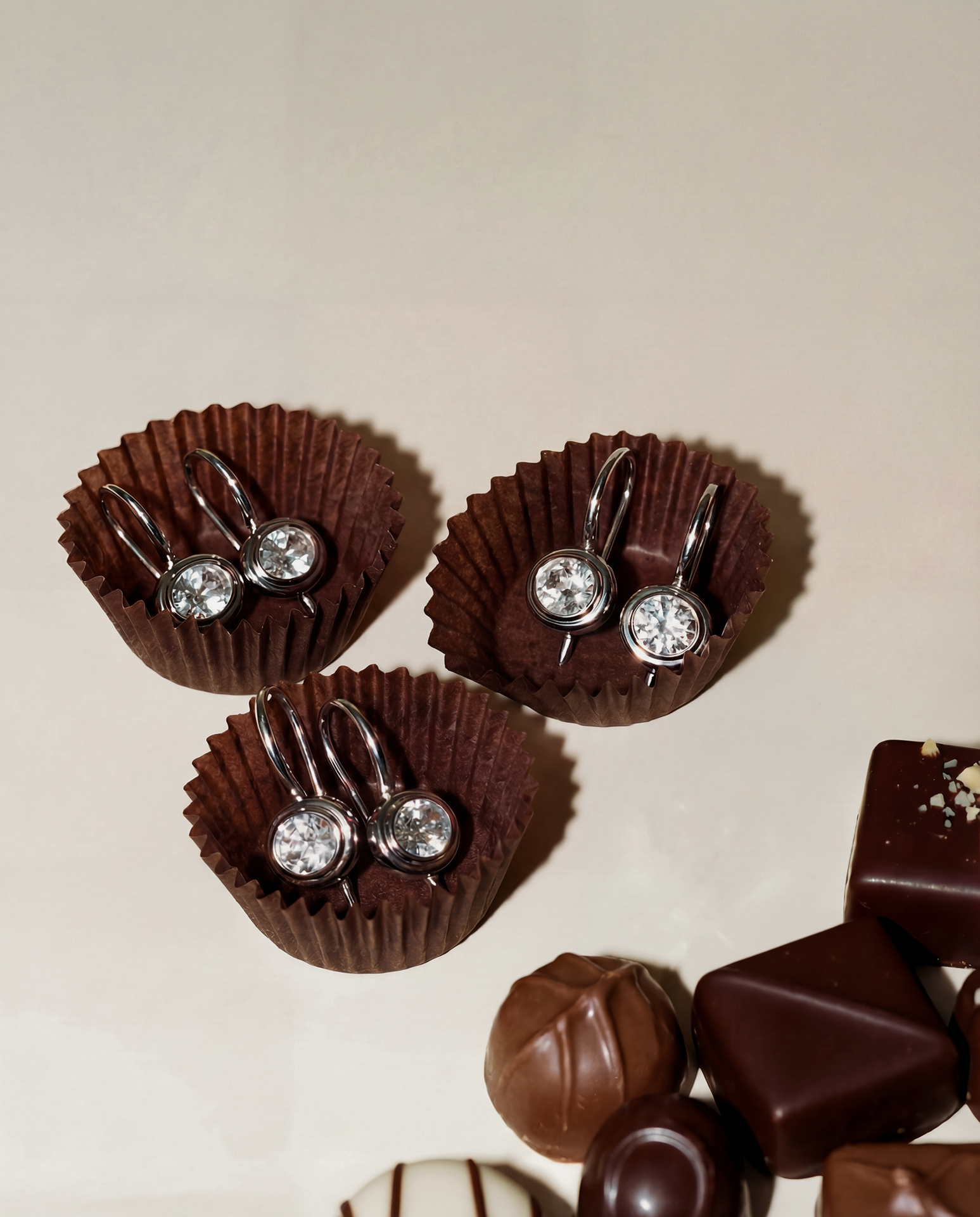 earrings in a little chocolate wrappers with additional chocolates on a beige background